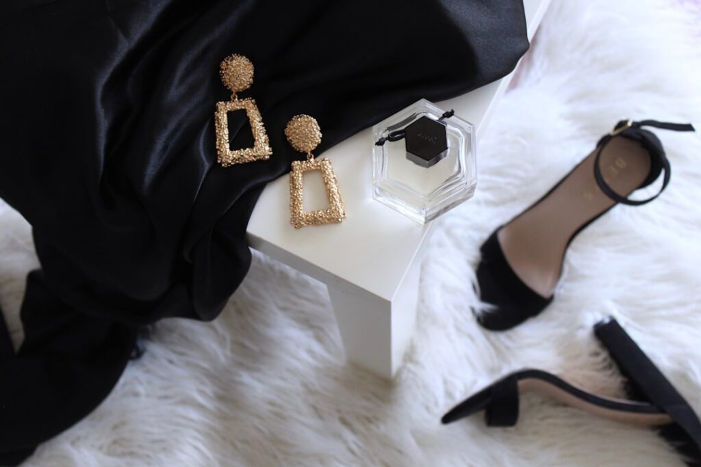 pair of gold colored earrings on table and black ankle strap pumps on area rug